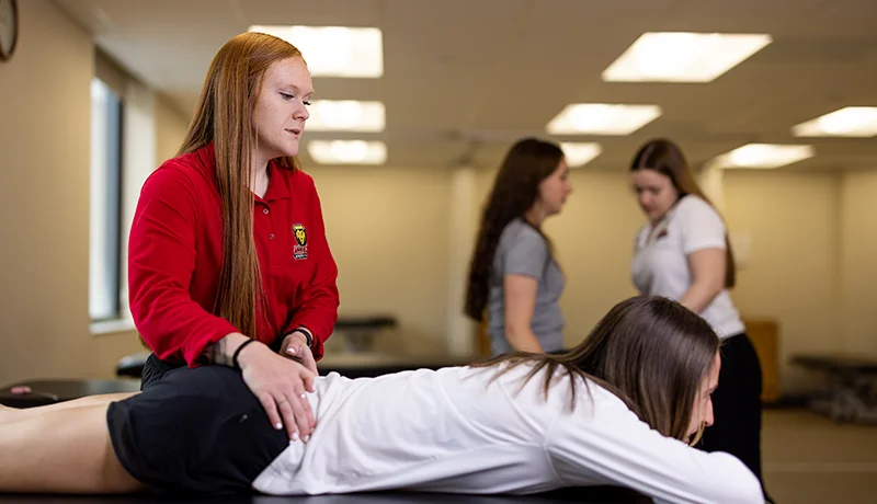 Female student practicing massage therapy on female client.