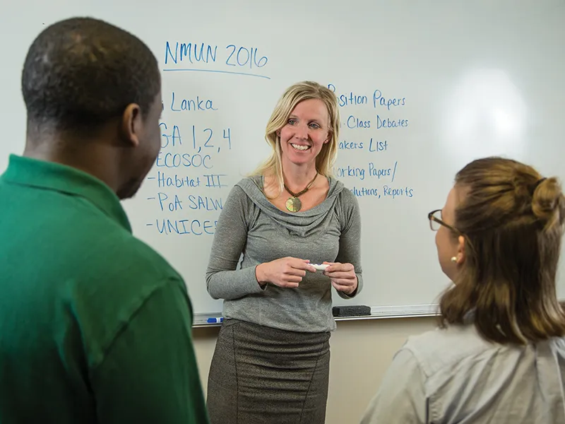 students and a professor talking in front of a whiteboard